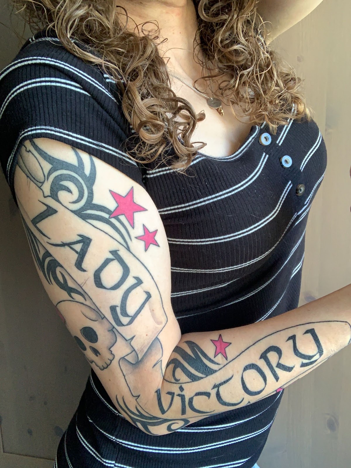 My right arm showing a tattoo: an old banner with the words LADY VICTORY on it, surrounded by a skull with a pink bow, five pink stars, and many sharp, curving lines. Full arm view.