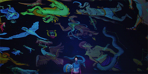 Animated gif of Maddy in the inflatable planetarium with images of constellations rotating behind her and projected onto her body and face from i Saw the TV Glow