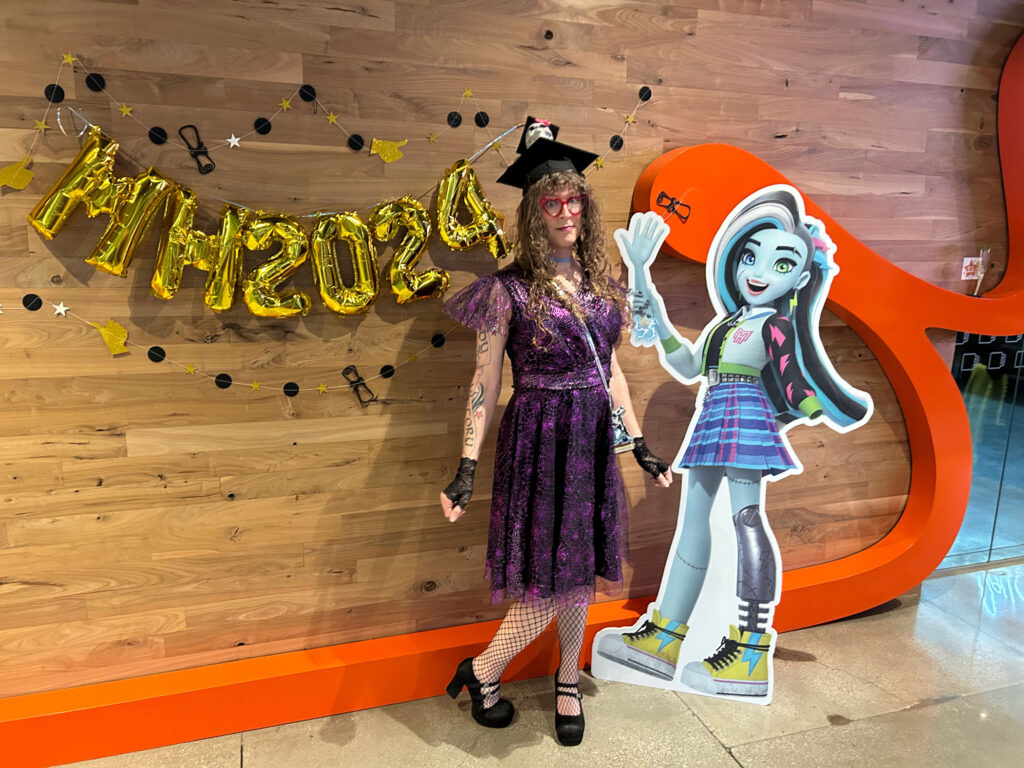 Me next to a Frankie cardboard standee, in front of balloons that say “MH2024”