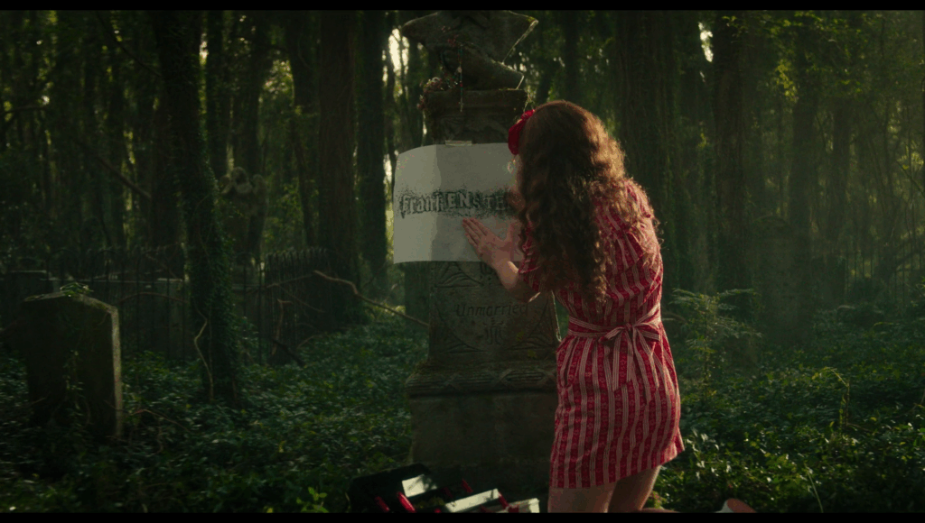 Lisa, dressed all in red, does a rubbing of Frank’s gravestone, in a cemetery inside a forest
