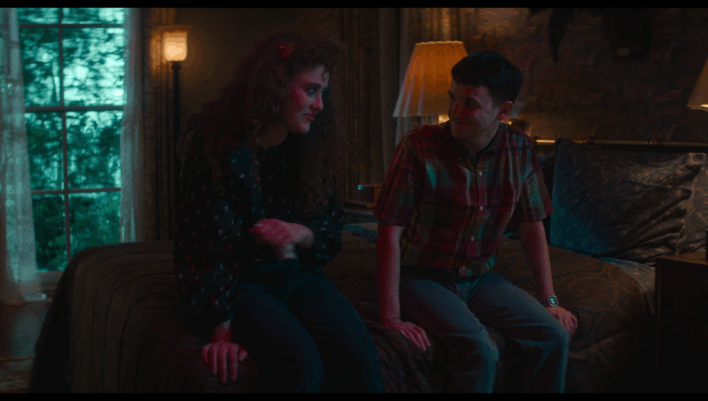 Lisa and Doug (I fuckin’ hate Doug) sit on a bed with yellow lights behind them, blue light shining on them, and a green-blue flash from lightning can be seen outside the window behind them.