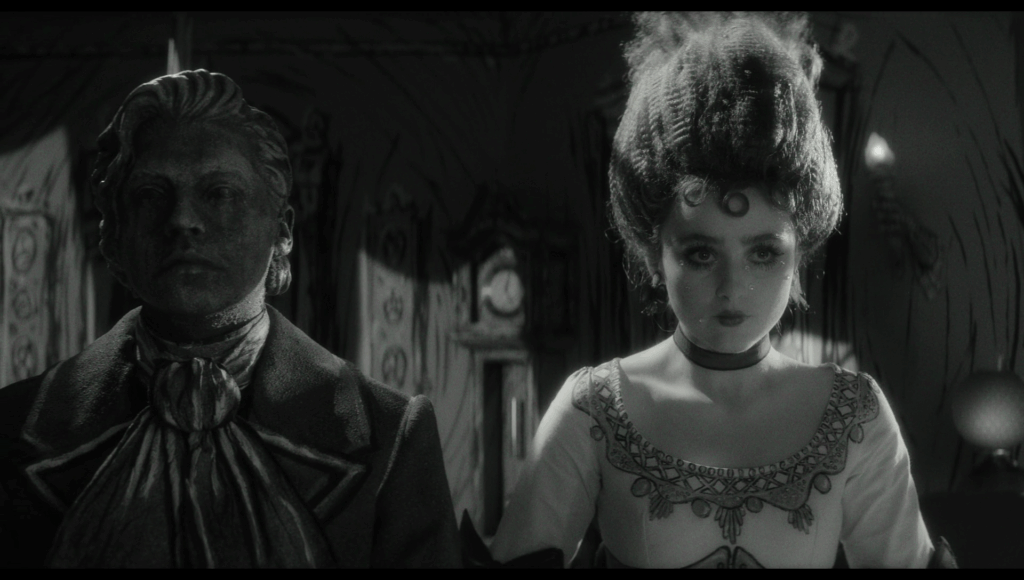 Black and white still of Frank, looking like a statue, sitting next to Lisa, looking like the Bride of Frankenstein.