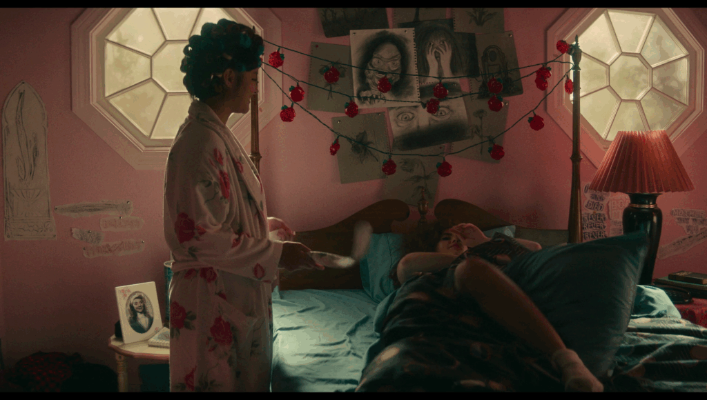 Lisa laying in bed, Taffy stands next ot the bed. Above the bed are two octagonal windows that look like eyes, and dysphoric black and white drawings that include a close up of terrified eyes, someone covering their face, and the creature from the black lagoon. On the far left is a drawing of… what looks like a penis.