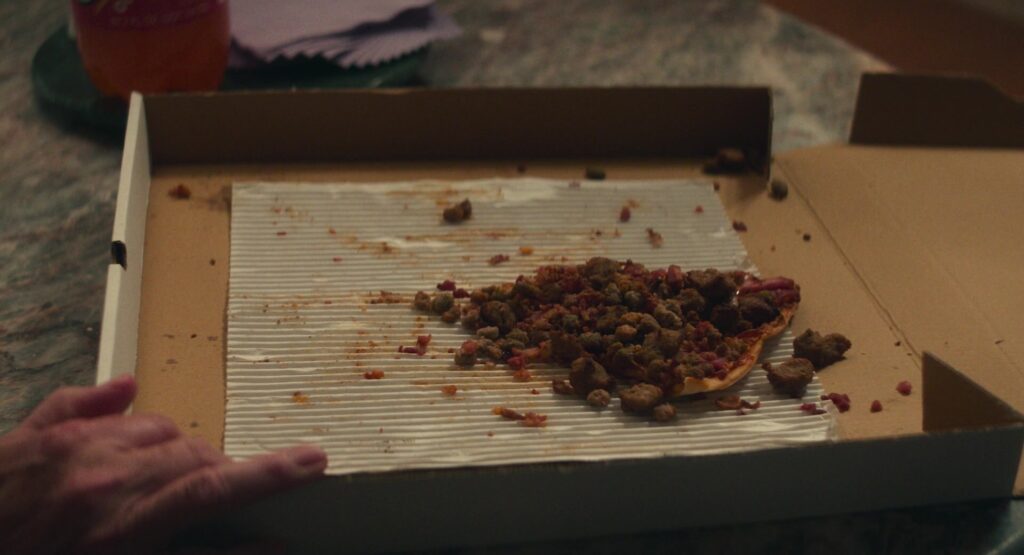 One slice of pizza in a pizza box, comically completely covered in meat.