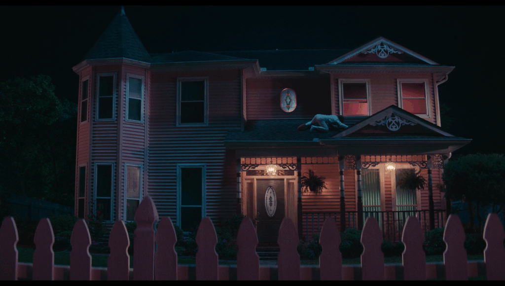 Lisa on the roof of a large, pink, two-story house after just climbing out of an upstairs window.