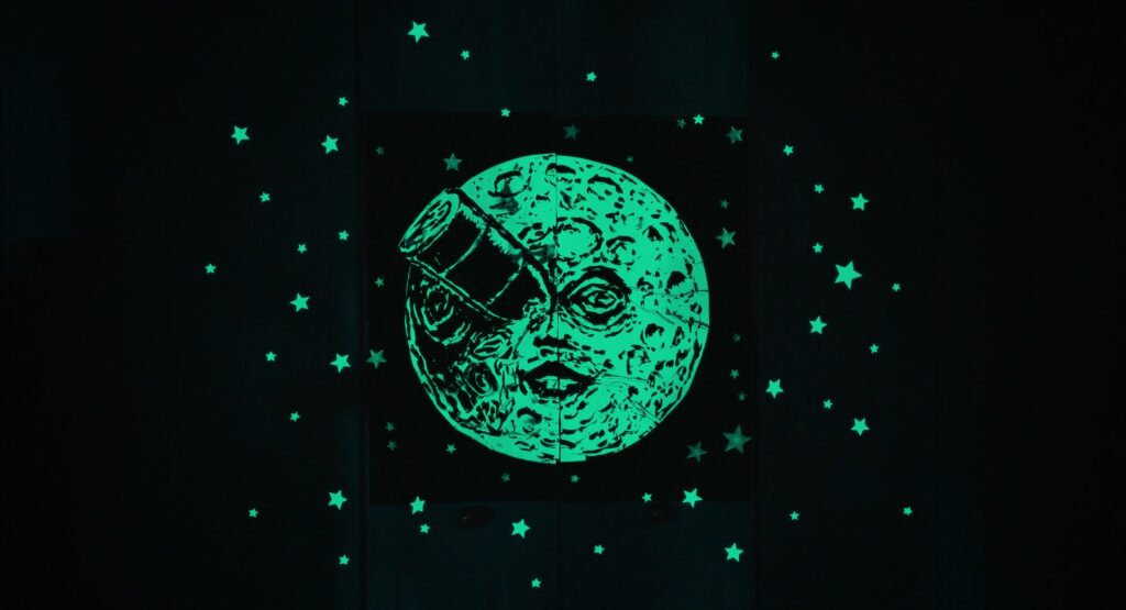 he man in the moon with a rocket in his eye, surrounded by stars, glowing green-blue in the dark