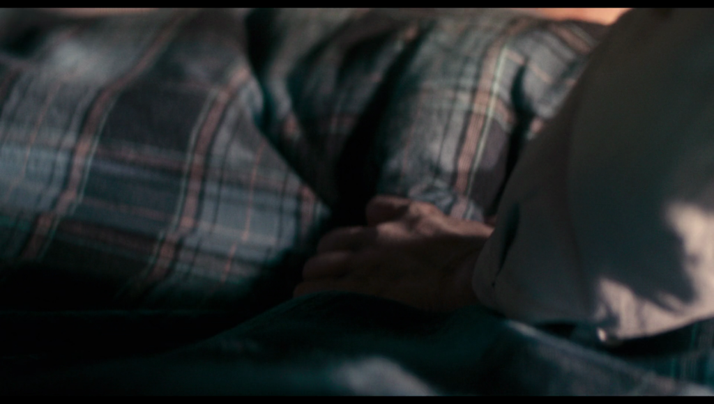 Frank’s hand pulling a pink and blue blanket off a bed.