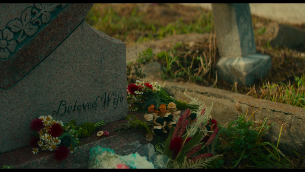 Red and white daisies at the base of Lisa’s tombstone, which is engraved with “beloved wife”