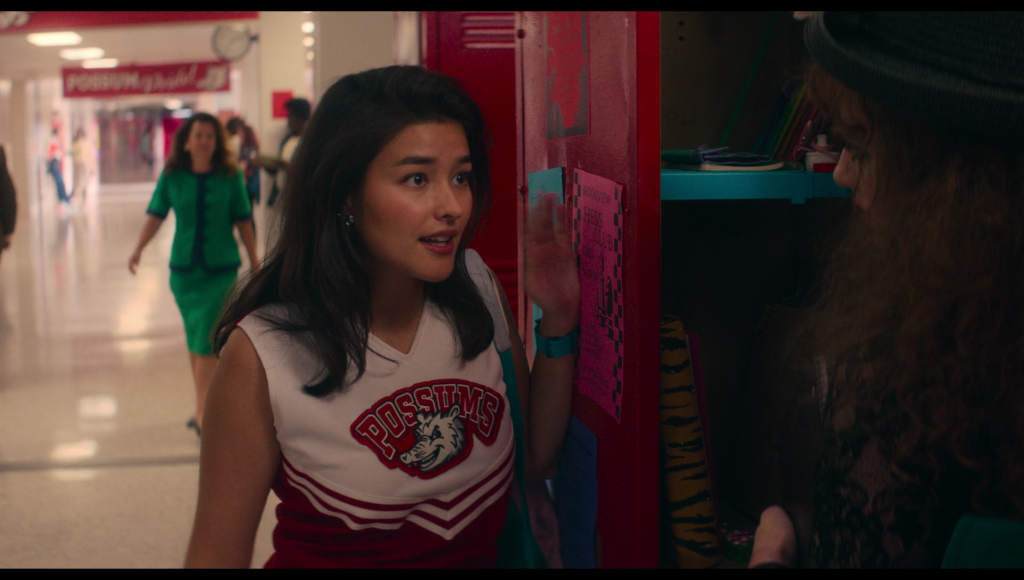 a woman in a green-blue dysphoria outfit walking in the background, as seen over Taffy's shoulder