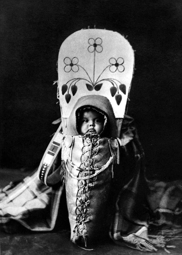 A black and white photo of a Native American baby in a papoose
