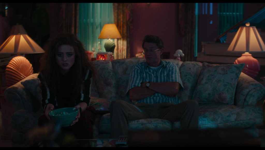 Lisa sits next to her dad on a sofa, looking miserable.