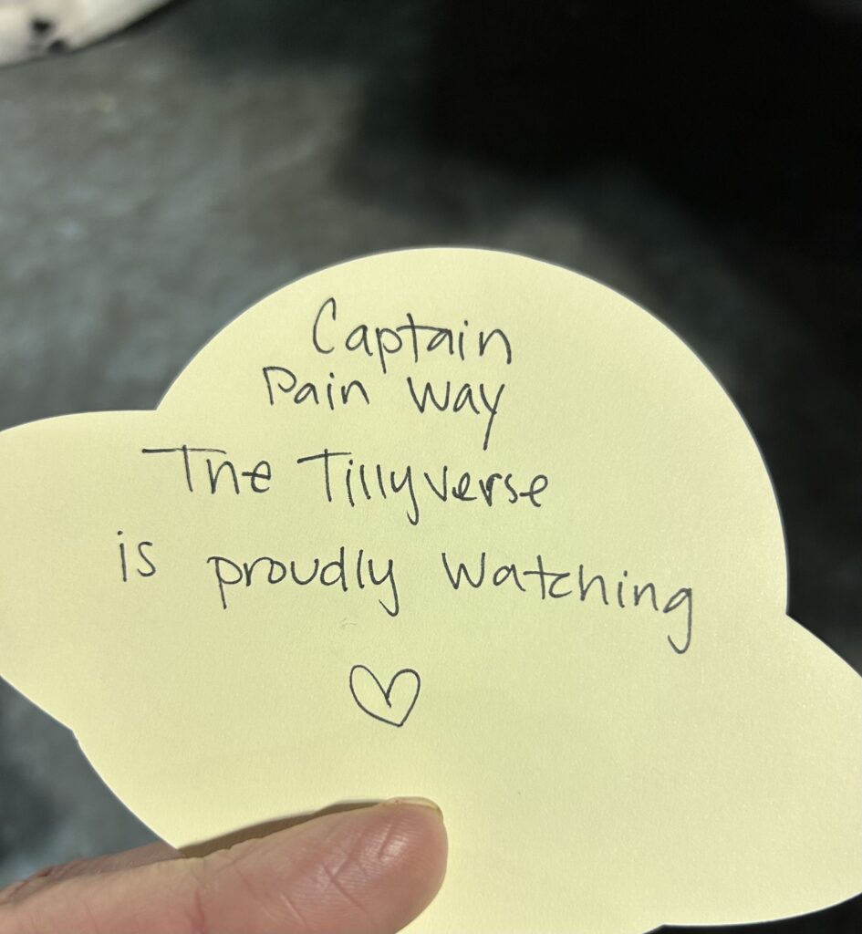 a handwritten note on the back of a card with an alien in a flying saucer that says "Captain Painway, the Tillyveryse is proudly watching" with a hand draswn heart