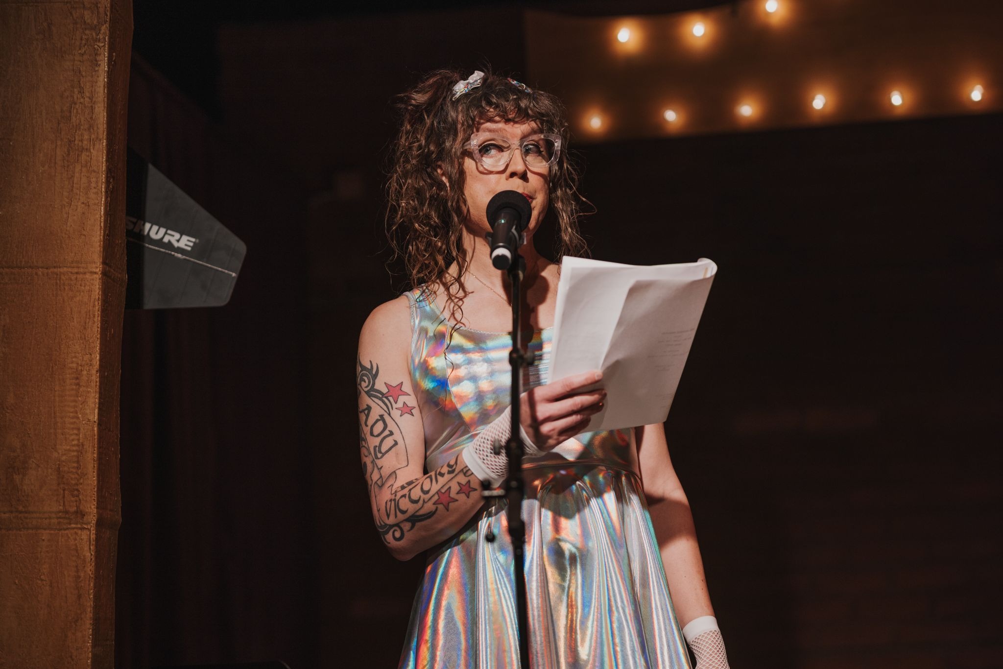 Me in a holographic dress, holding a script, on stage speaking into a microphone